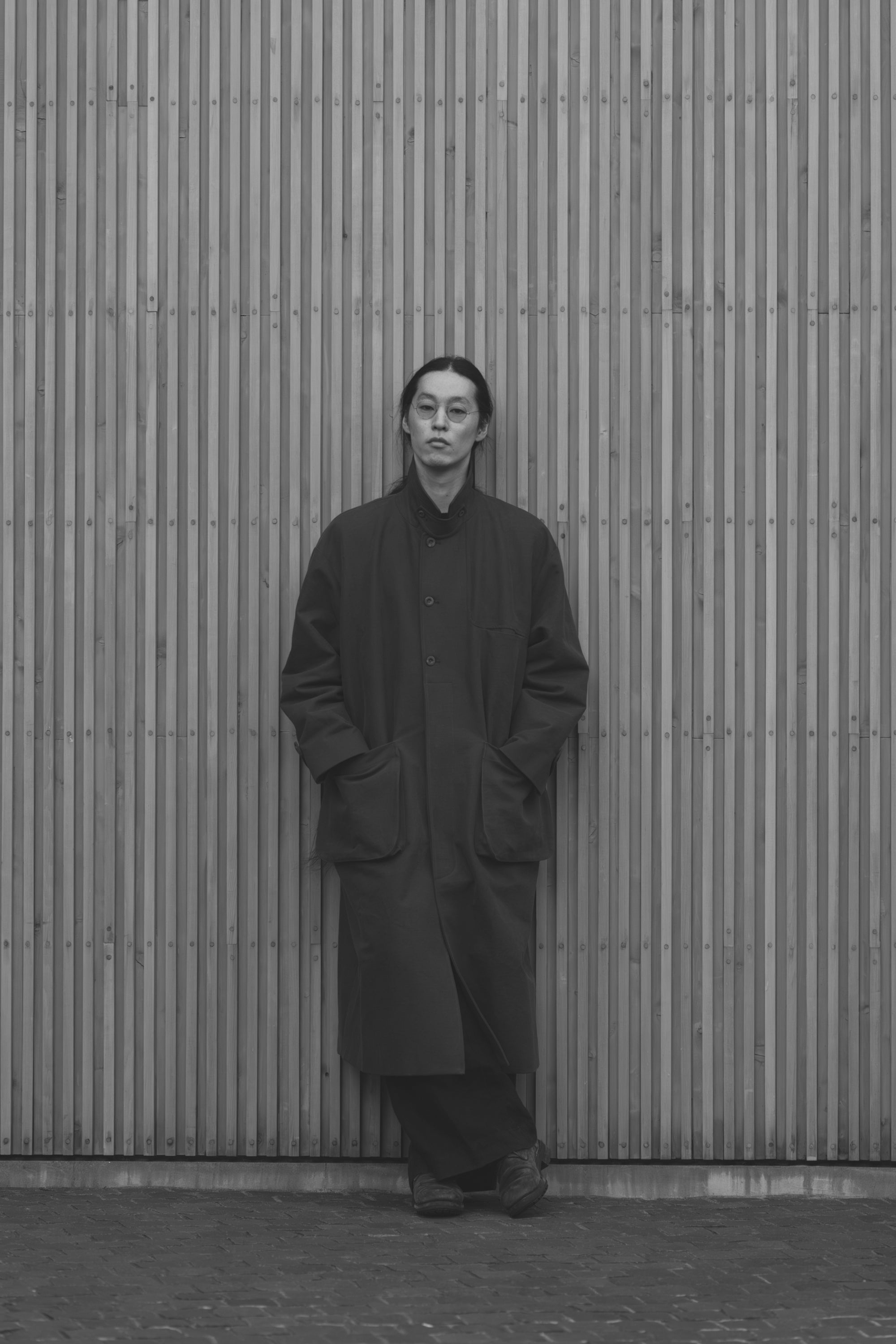 Modelo apoyada en una pared con el Aviva Jifei Xue Relaxed Mac Coat con el cuello levantado