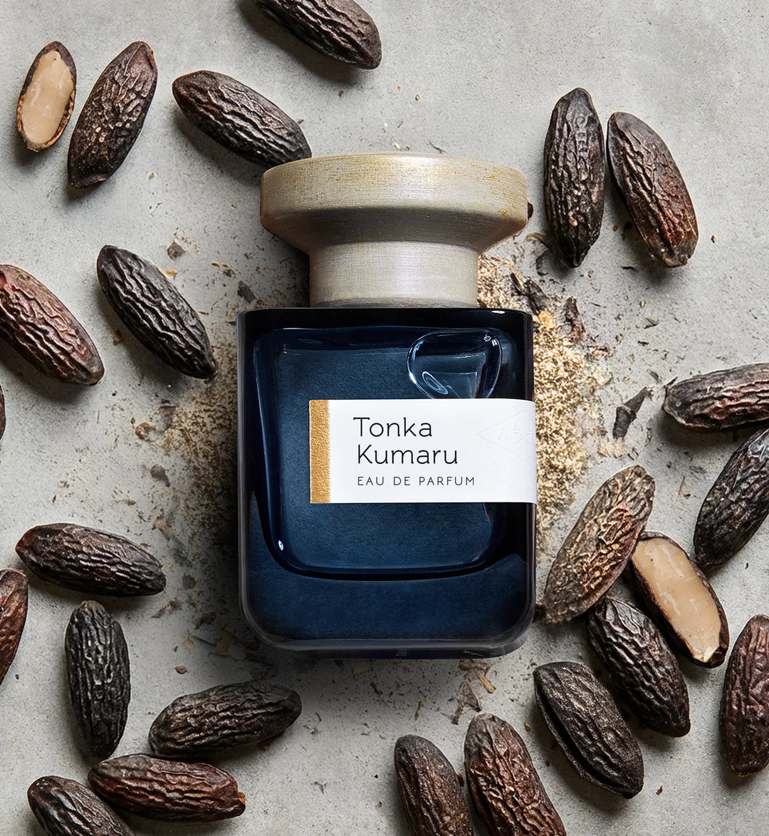 Una foto del flacone di ATELIER MATERI Tonka Kumaru accanto a fave tonka.